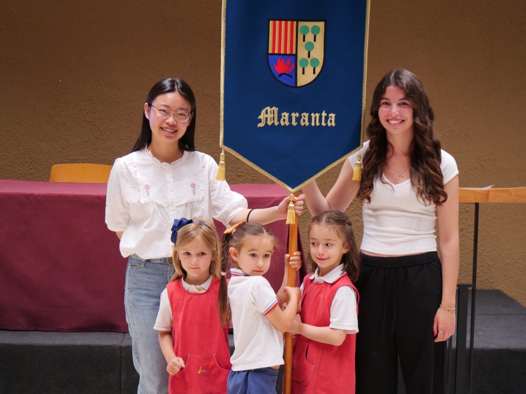 En Pineda, cada promoción tiene un nombre que pasa de generación en generación. Cuando las alumnas de 2º de Bachillerato terminan su etapa en el colegio, entregan su estandarte a las niñas que comenzarán 1º de Primaria el curso siguiente, manteniendo así viva una tradición muy especial que une a todas las promociones.
Las niñas de Avantis han llegado puntualísimas y se han sentado en la sala de actos dejando huecos entre ellas para las alumnas mayores de Pineda, que han entrado con muchísima ilusión mientras las pequeñas las esperaban cantando el himno de Avantis.
Durante el acto, la directora, Elisa Comes, ha explicado a las niñas el importante paso que están a punto de dar y el significado del nombre de su promoción. Después, una a una, las alumnas de I5 han sido nombradas para recibir un punto de libro de Pineda como recuerdo de este día tan especial.
Finalmente, las secretarias de curso han dedicado unas palabras a las niñas y han hecho entrega del estandarte Maranta a tres alumnas de I5 de Avantis. El acto ha terminado con todas cantando juntas el himno de Pineda y con una preciosa foto de las dos promociones Maranta.